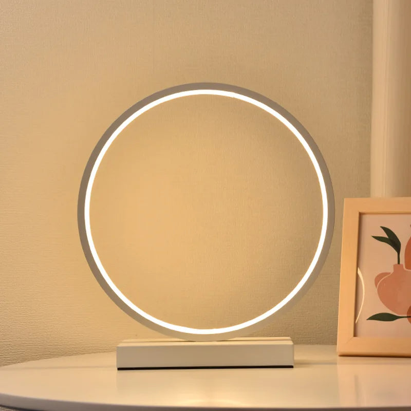 Moderne Luce dell'Anello Nachttischlampe mit kreisförmigem LED-Licht und minimalistischem Design auf einem Nachttisch.