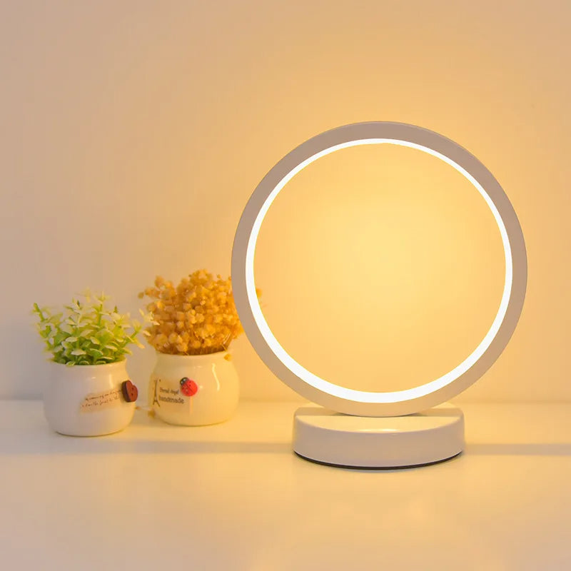 Moderne Luce dell'Anello Nachttischlampe mit kreisförmigem LED-Licht und minimalistischem Design auf einem Nachttisch.